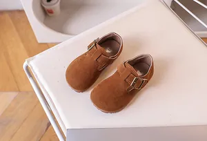 Détail de chaussures en daim marron pour enfants avec boucle en bronze et semelle cœur