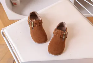 Détail de chaussures enfants en daim caramel avec boucle vintage sur coussin blanc