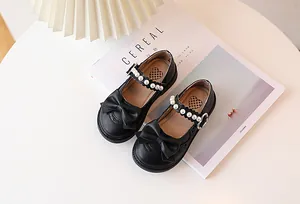 Detail of girls' black Mary Jane shoes with pearls, bow, and heart buckle on a magazine