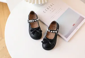Detail of girls' black Mary Janes with bow, pearl strap, and wavy lace edge