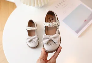 Detail of girls beige Mary Jane shoes with bow, pearl strap and heart cut-outs