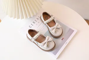 Detail of girls' cream Mary Janes featuring a pearl strap and bow on a white table