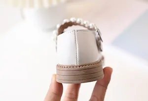 Close-up of girl's white Mary Jane leather shoes with elegant pearl strap and anti-slip sole