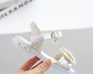Close-up of holographic silver girl's sandals with pearl bow and velcro strap detail