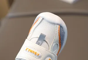 Détail de chaussure de marche bébé avec maille respirante, coutures orange et velcro