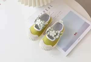 Detail of mustard green canvas toddler shoe with bow decoration and white flower accent
