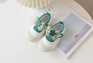 Detail of children's white Mary Jane canvas shoes with green trim and plaid bow decoration