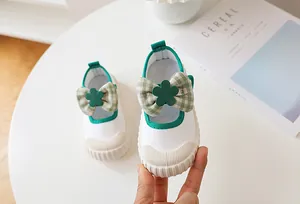 Detail of white canvas toddler shoe with green plaid bow and non-slip rubber toe cap