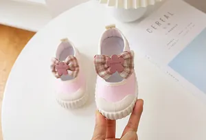 Detail showing pink canvas kids shoe with plaid bow, rubber toe cap and floral decoration