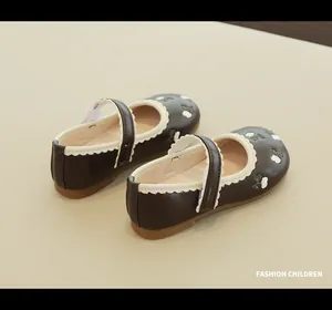 Close-up of children brown leather Mary Janes with white flower embroidery and wavy trim