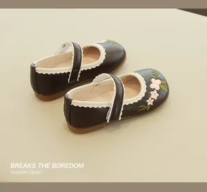 Detail of girls' brown Mary Jane shoes with pink floral embroidery and scalloped trim