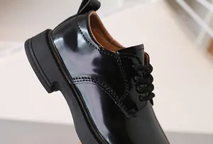 Detailed view of kids' black patent leather derby shoes with laces and stitching