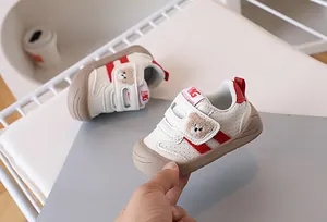 Detail of beige baby walking shoes with plush bear patch and red side stripes