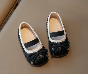 Close-up of glittery black Mary Janes for girls with white scalloped trim and bow detail