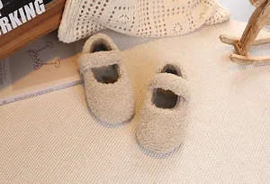 Close-up of beige plush Mary Jane baby shoes with soft fleece texture in a cozy setting
