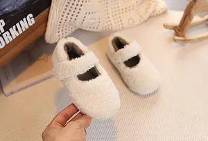 Close-up of cream fuzzy Mary Jane baby shoes with adjustable velcro strap and soft plush texture