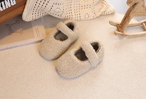 Top-down view of cozy beige plush Mary Jane baby shoes on a woven carpet with wooden props