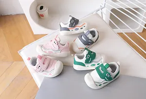 Three pairs of dinosaur-themed baby walking shoes in pink, green, and grey on a wooden floor