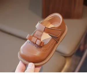 Détail de chaussure Mary Jane marron avec nœud et découpes brogue tenue à la main