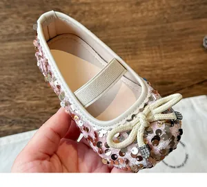 Detailed close-up of girls' pink sequin flat shoes with a woven bow and sparkling gems