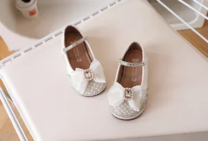 Détail de babies crème pour filles avec nœud en dentelle, perles et strass scintillants