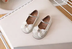 Détail de chaussures Mary Jane blanches avec paillettes, nœud en dentelle et boucle en perle