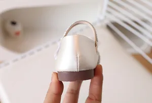 Gros plan de chaussures Mary Jane blanches pour enfant avec nœud brillant et couture