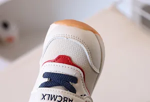 Dettaglio scarpa primi passi in pelle beige con punta rossa e lacci blu scuro per neonati
