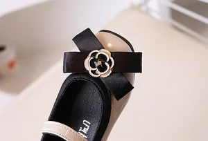 Close-up of girl's beige Mary Janes with black satin bow and camellia flower detail