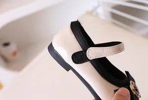 Detail view of beige patent leather girl shoes with camellia flower and velcro strap