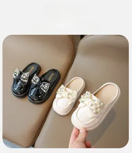 Close-up of girls' patent leather clogs featuring pearl-encrusted bows in black and cream