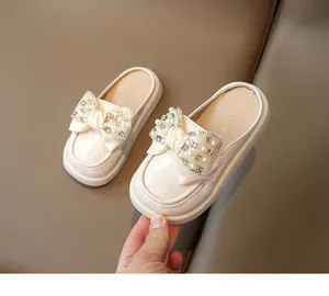 Detailed shot of cream patent leather girls' mule with large pearl and rhinestone bow