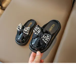 Detail of girls' black patent leather mules featuring a lace bow with pearls and rhinestones