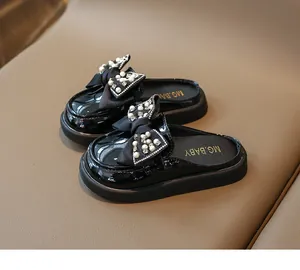 Close-up of black patent leather girls' mule shoes with pearl and rhinestone bow detail