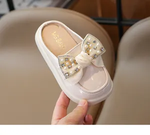 Detail of girls beige patent leather mules with a satin bow and pearl rhinestone accents