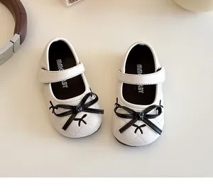 Close-up of white Mary Jane girl shoes with black bow and quilted leather texture