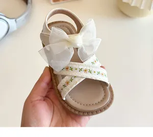 Détail de sandales fille avec nœud en organza blanc et broderies florales sur brides