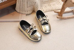 Dettaglio di scarpe Mary Jane dorate metallizzate con doppio fiocco su tappeto