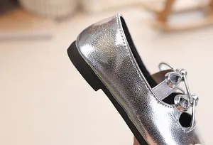 Dettaglio di scarpe da principessa argento glitterate per bambine con fiocco decorativo