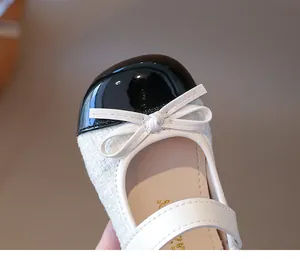 Detailed close-up of girls' black patent leather toe with white tweed and bow tie detail