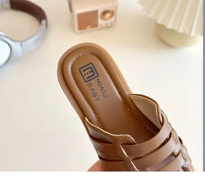 Gros plan de sandales pour enfants en cuir tressé caramel sur fond crème chaleureux