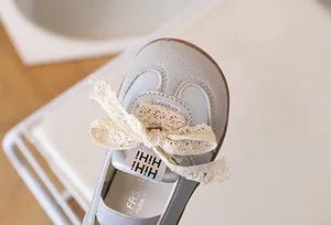 Dettaglio di sneaker grigie da bambina con fiocco in pizzo e finitura opaca fine