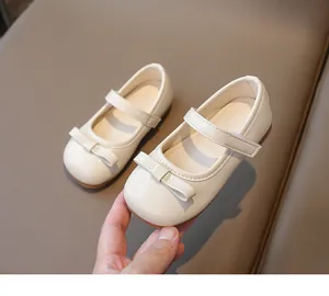 Detail of cream Mary Jane shoe with bow knot and velcro strap held by a hand