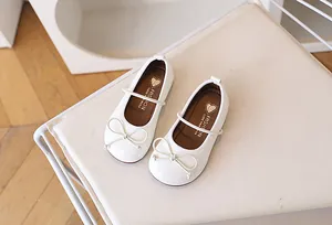 Detalle de merceditas en charol blanco con un lazo fino y motivo de corazón infantil