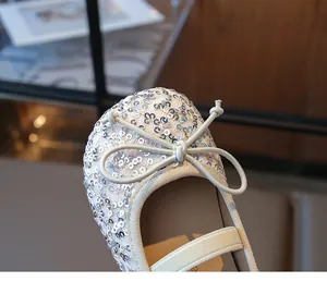 Macro shot of silver sequined ballet flat shoe featuring white bow and elastic strap
