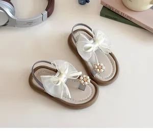 Detail of beige girls sandals with white lace bow, pearl accents and anti-slip sole