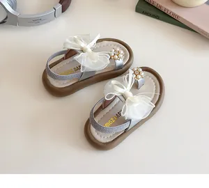 Close-up of baby girl sandals with mesh bow and pearl floral detail on beige surface