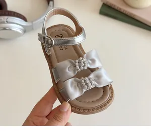 Detailopname van zilveren meisjessandalen met strass-strikken en zachte rubberen zolen