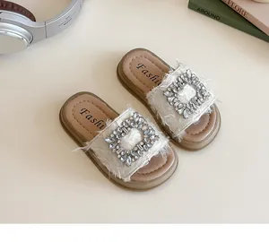 Detalle de sandalias crema para niñas con hebilla de pedrería y adornos de flecos