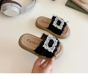 Detalle de sandalias negras para niñas con flecos y una gran hebilla cuadrada de pedrería
